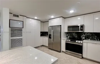 Kitchen featuring sleek white flat-panel cabinetry, light-toned stone-finish countertops, stainless steel appliances, and a high-contrast dark stone backsplash