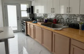 Kitchen featuring high-gloss white upper cabinetry, wood-surface countertops, mosaic tile backsplash, stainless steel appliances, and large-format porcelain tile flooring