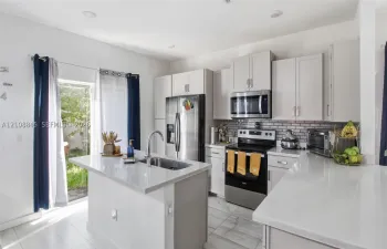 Kitchen featuring light-toned cabinetry, quartz countertops, subway tile backsplash, stainless steel appliances, and a central island with an integrated sink