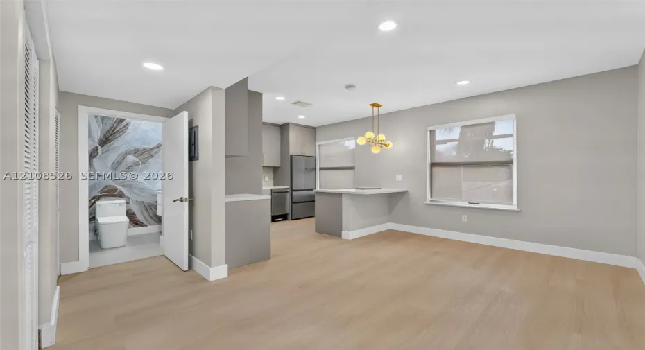 Open-concept interior featuring light wood-finish flooring, recessed lighting, a kitchen peninsula with integrated counter seating, and a modern multi-globe chandelier