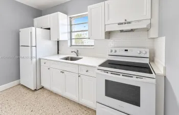Kitchen featuring white shaker-style cabinetry, solid-surface countertops, a subway tile backsplash, terrazzo flooring, and stainless steel undermount sink