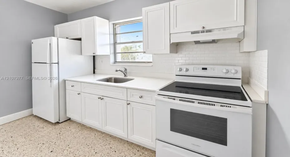 Kitchen featuring white shaker-style cabinetry, solid-surface countertops, a subway tile backsplash, terrazzo flooring, and stainless steel undermount sink