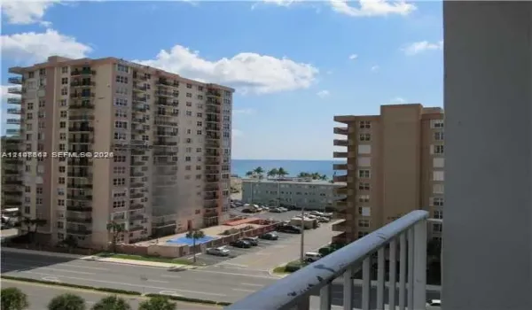 Exterior balcony featuring a metal railing and an outlook toward the ocean, neighboring high-rise structures, and street-level hardscaping