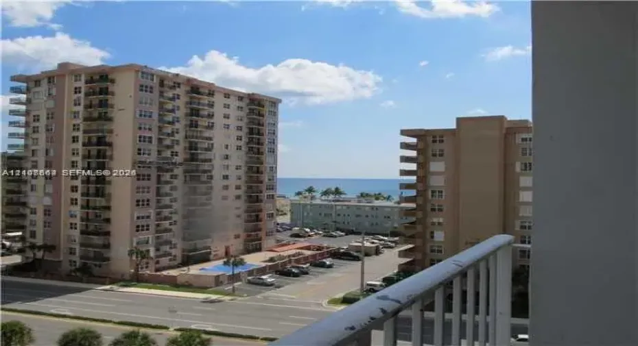 Exterior balcony featuring a metal railing and an outlook toward the ocean, neighboring high-rise structures, and street-level hardscaping