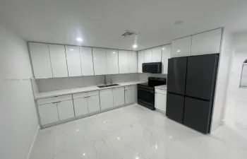 Kitchen featuring gloss-finish white cabinetry, stone-surface countertops, subway tile backsplash, oversized light-colored floor tiles with vein detailing, and integrated black appliances
