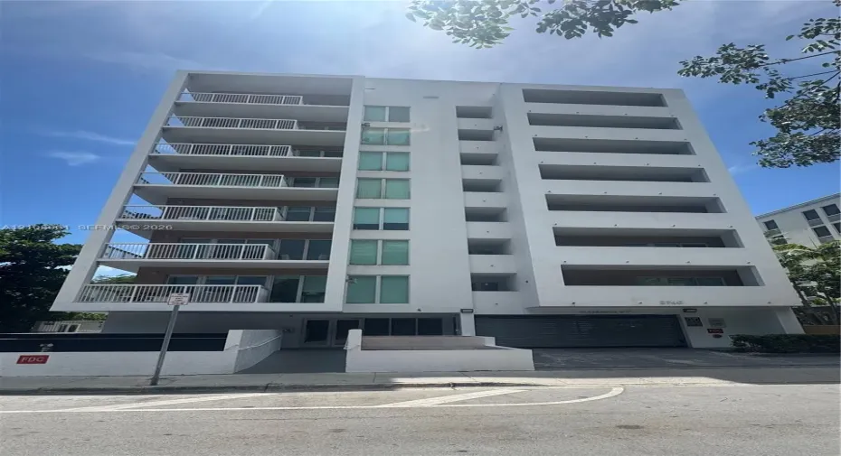 Multi-story high-rise exterior featuring white stucco facade, private recessed balconies, and integrated garage access