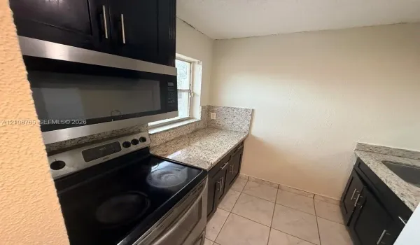 Kitchen featuring dark cabinetry, stone countertops, stainless steel appliances including a built-in microwave and range, and tiled flooring