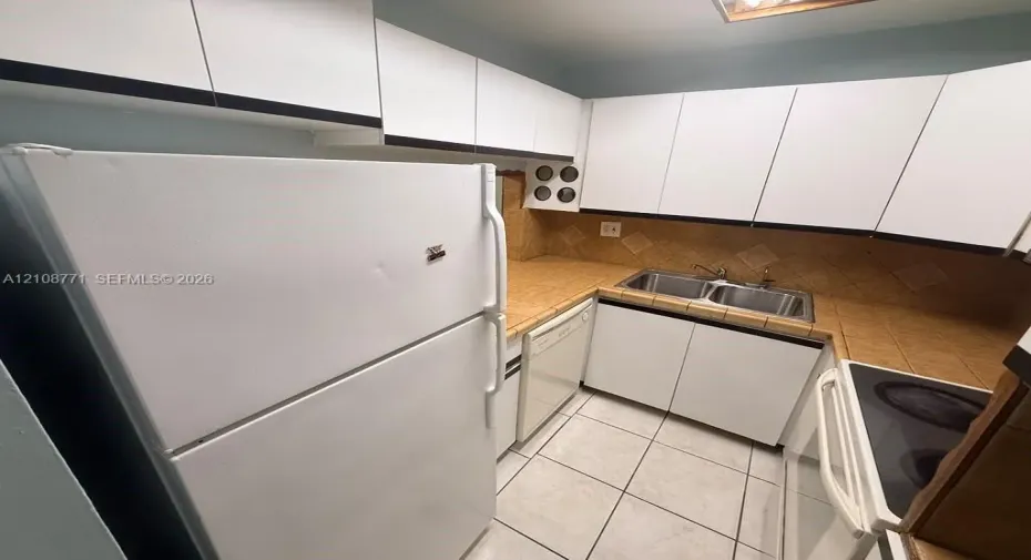 Kitchen featuring white cabinetry, tile countertops, tile backsplash, tile flooring, and a stainless steel double-basin sink