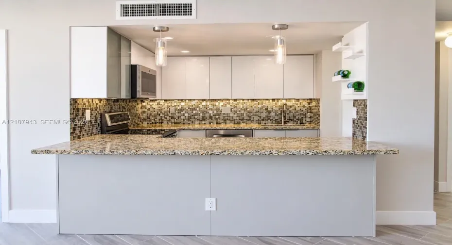 Kitchen featuring a stone countertop peninsula, white flat-panel cabinetry, mosaic tile backsplash, stainless steel appliances, and pendant lighting