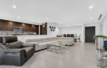 Open-concept space featuring large-format tile flooring, recessed ceiling lighting, dark cabinetry, and a decorative tile backsplash