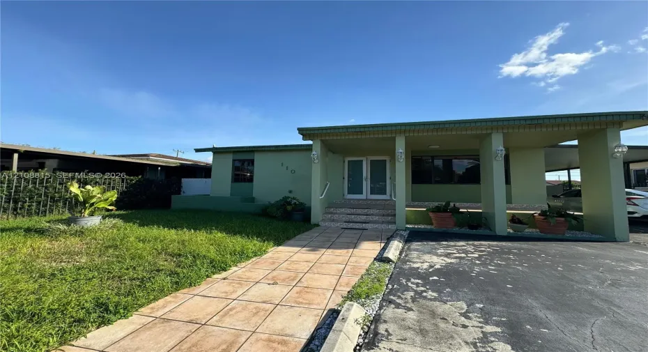 Single-story exterior featuring a covered front porch, double-door entryway, tile walkway, and an attached carport