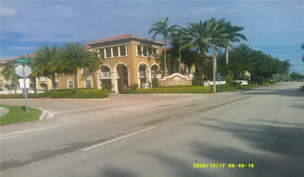 Multi-story stucco exterior with arched porticos, tile roof, and mature palm tree landscaping