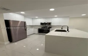 Kitchen featuring white high-gloss cabinetry, stone-finish countertops, stainless steel appliances, a center island with an undermount sink and matte black faucet, and large-format porcelain tile flooring