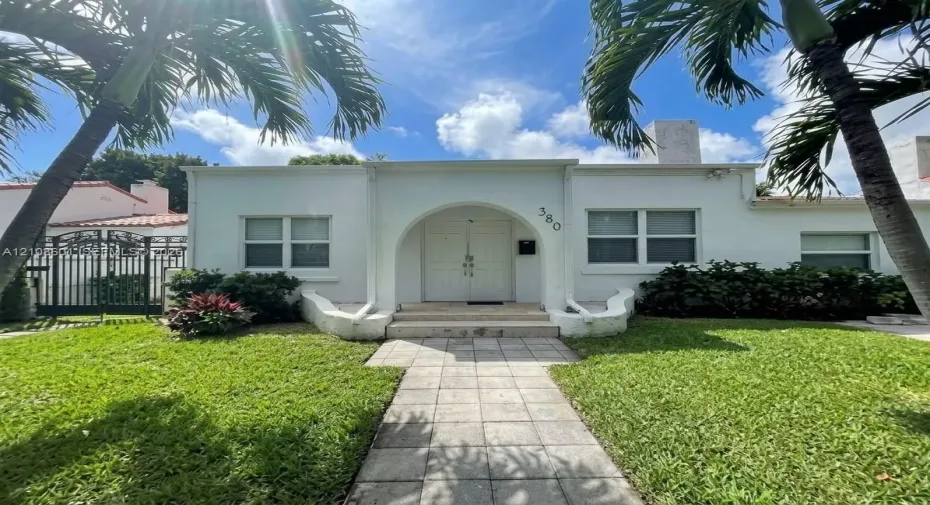 Stucco exterior featuring an arched entryway, double-door entrance, stone-paved walkway, and manicured landscaping
