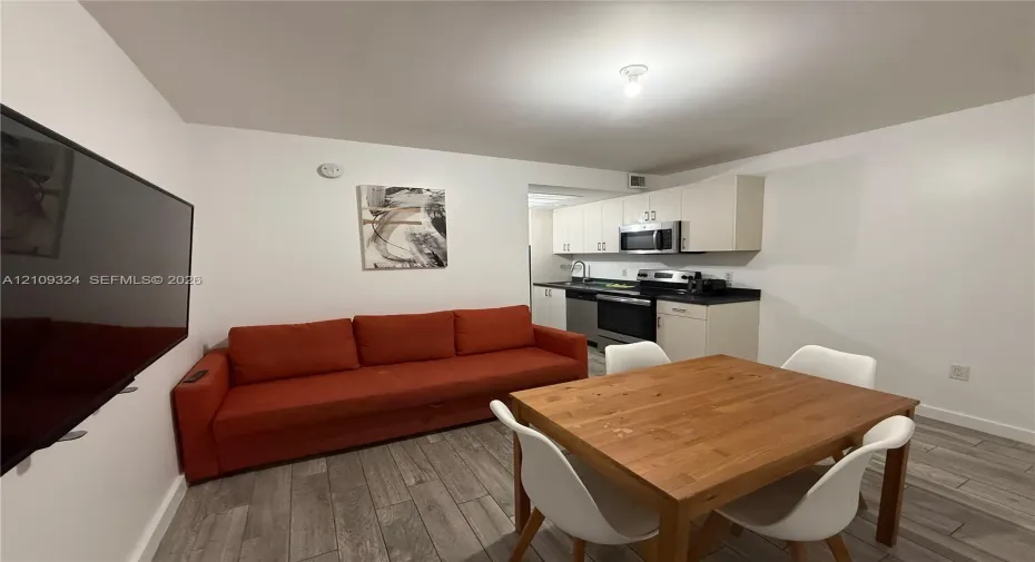 Kitchen featuring light-finish cabinetry, dark solid-surface countertops, and stainless steel appliances, complemented by wood-finish flooring