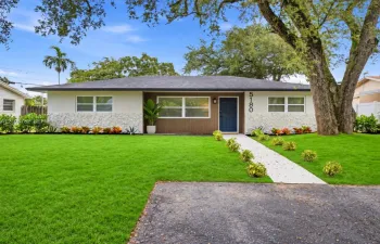 Single-story exterior featuring light-toned textured stone accents, a deep-toned shingled roof, a central entry with a paneled door, and a concrete walkway
