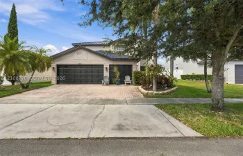 Multi-level exterior featuring a metal roof, paver driveway, three-car garage with dark-finish doors, and landscaped garden beds