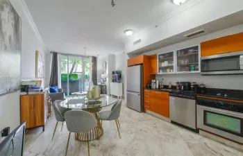 Open-concept kitchen featuring warm-toned flat-panel cabinetry, dark stone countertops, stainless steel appliances, and tile flooring throughout