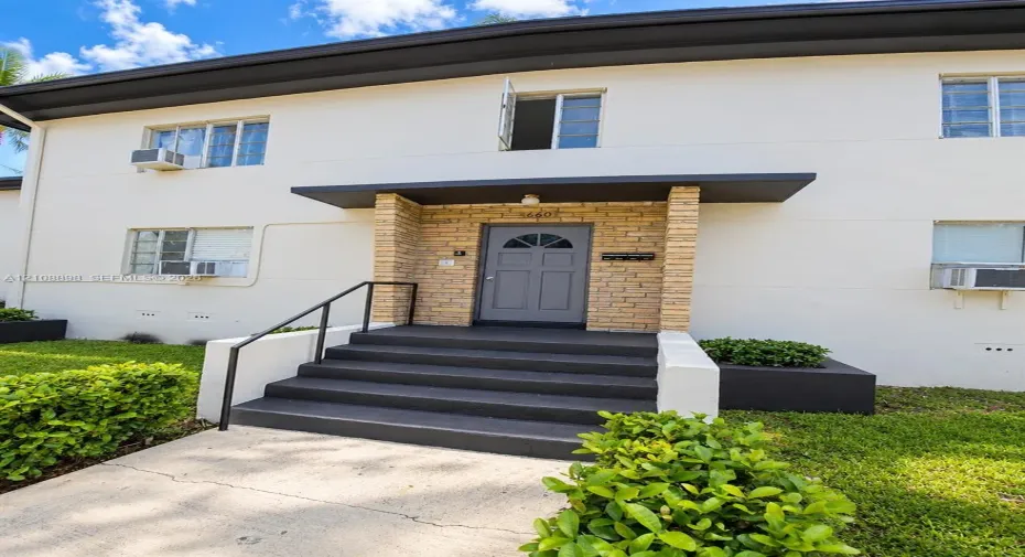 Exterior facade featuring a smooth stucco finish, stone-veneer entryway accents, gray-painted concrete stairs with metal handrails, and built-in landscape planters