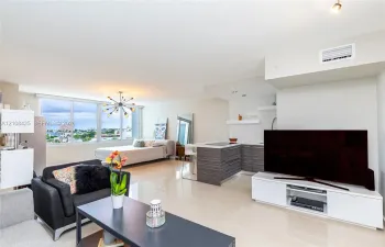 Open-concept interior featuring large-format polished tile flooring, floor-to-ceiling windows, and a kitchen with horizontal-grain cabinetry and a breakfast bar