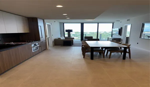 Modern kitchen featuring wood-finish cabinetry, built-in stainless steel oven, stone-surface countertops, recessed ceiling lighting, and floor-to-ceiling glass doors opening to a private balcony