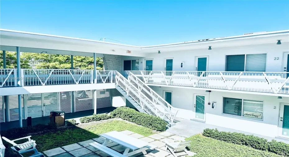 Two-story exterior with white facade, metal staircase, expansive central courtyard, stone-texture siding accents, and paver-stone ground surfacing