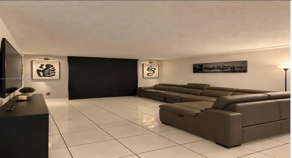 Large-format square floor tiles, wall-mounted picture lighting, and opaque window shades