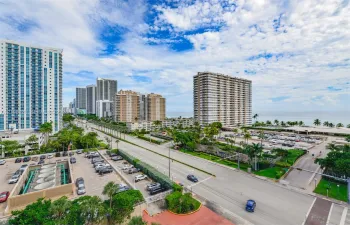 Aerial perspective of a coastal corridor featuring high-rise architecture, multi-lane roadways, mature palm trees, and proximity to the oceanfront