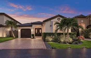 Single-story exterior featuring a tile roof, decorative double entry doors with glass inserts, brick-paver driveway, and professional landscape design