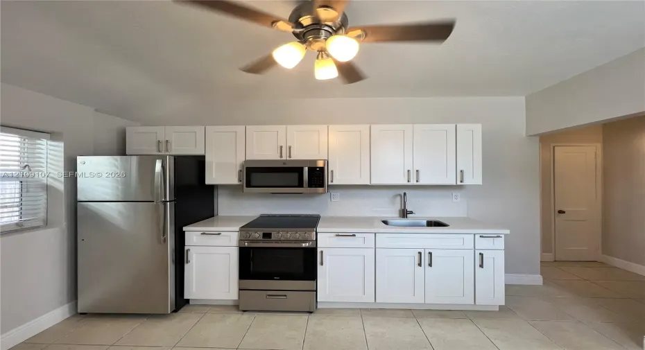 Kitchen featuring white shaker-style cabinetry, stainless steel appliances, neutral countertops, and tile flooring