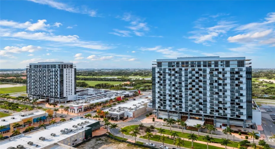 High-rise urban development featuring staggered balcony architectural detailing, expansive multi-story structural design, integrated street-level commercial space, and manicured tropical landscaping