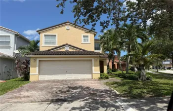 Two-story stucco exterior featuring a tiled roof, attached two-car garage, and a decorative brick-paver driveway