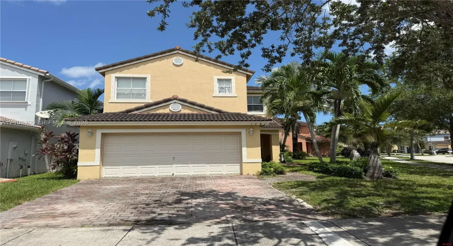Two-story stucco exterior featuring a tiled roof, attached two-car garage, and a decorative brick-paver driveway