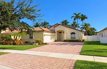 Stucco exterior residence featuring a multi-gabled tile roof, paver driveway, arched entryway, and established palm trees