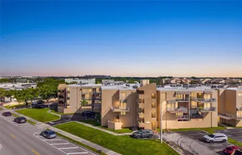Multi-story residential complex featuring stucco exterior walls, private balconies with metal railings, and asphalt parking areas