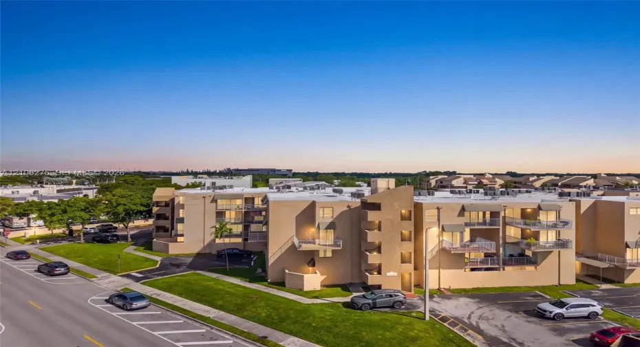 Multi-story residential complex featuring stucco exterior walls, private balconies with metal railings, and asphalt parking areas