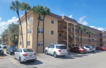 GARDENS AT LAUDERHILL Multi-story exterior featuring a stucco facade, dark-toned shingled roof, metal railings, and mature palm trees