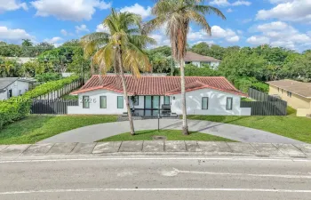 Single-story exterior featuring a terracotta tile roof, white stucco facade, semicircular concrete driveway, and vertical panel fencing