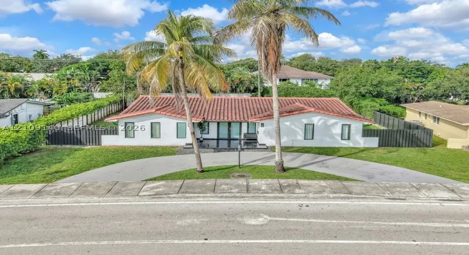 Single-story exterior featuring a terracotta tile roof, white stucco facade, semicircular concrete driveway, and vertical panel fencing