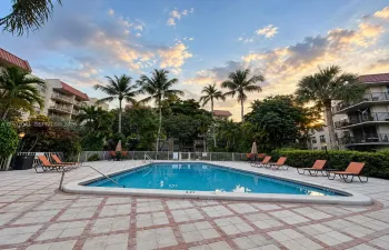 Outdoor swimming pool with decorative tile coping, surrounded by a paved deck featuring stone-look pavers with brick-style trim