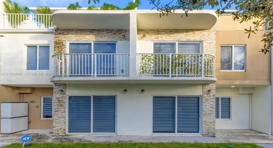 Multi-level exterior featuring stacked stone veneer, private upper-level balcony with metal railings, and dual-level sliding glass doors