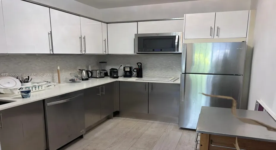 Kitchen featuring white upper cabinetry, stainless steel lower cabinets, light-toned countertop, textured backsplash, and stainless steel appliances