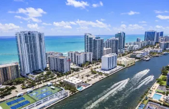Aerial perspective of coastal high-rise development featuring waterfront proximity, hardscaped recreation courts, and open water access