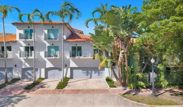 Three-story exterior featuring a terracotta tile roof, white stucco facade, multiple private balconies with metal railings, and attached multi-car garages with paver driveways