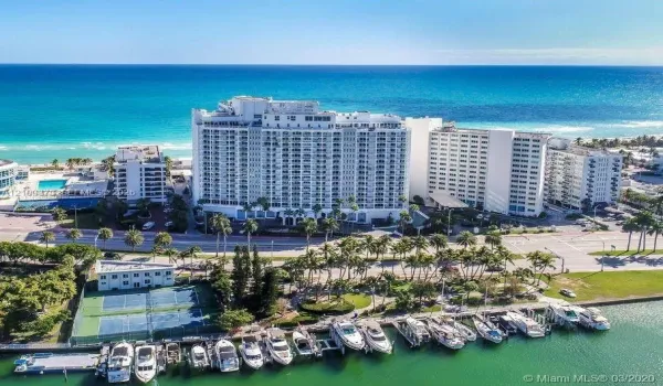 Aerial perspective featuring waterfront high-rise residential architecture, private deep-water boat slips, tennis courts, and palm-lined landscaping