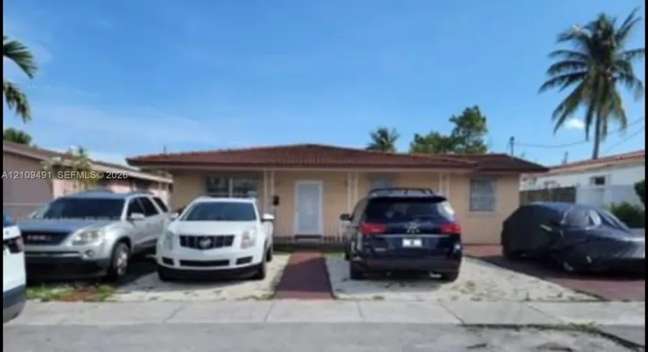 Single-story residence featuring a low-slope roof with barrel-style tiles, concrete exterior, and a multi-car parking area