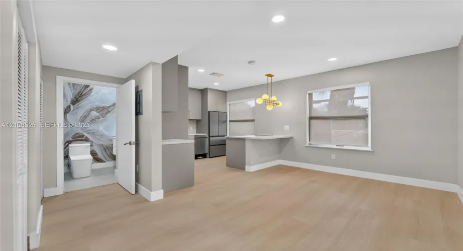 Open-concept interior featuring light wood-finish flooring, recessed lighting, a kitchen peninsula with integrated counter seating, and a modern multi-globe chandelier