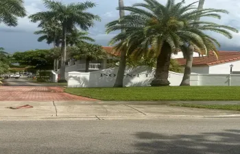Stucco monument signage featuring mature palm trees, tile roof structures, and paved brick driveway