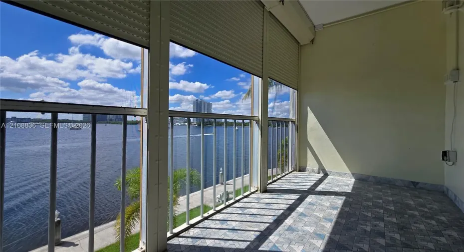 Enclosed balcony featuring patterned tile flooring, metal railings, and retractable exterior security shutters