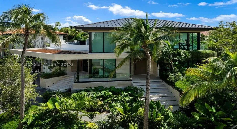 Contemporary residence featuring floor-to-ceiling glass windows, stone cladding, a standing-seam metal roof, integrated glass terrace railings, and stone staircases